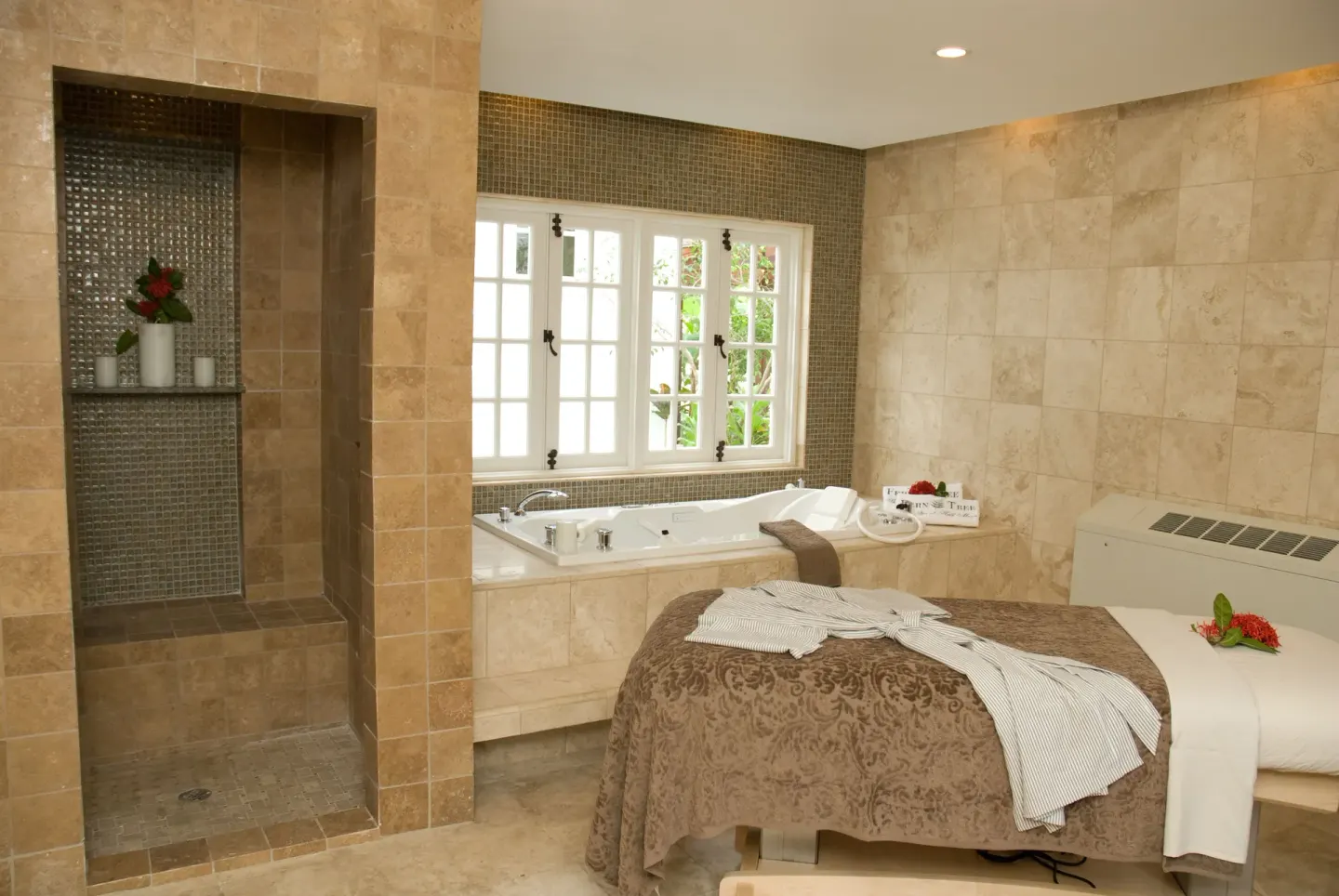A tiled spa treatment room with massage table, shower, and soaking tub at Half Moon.
