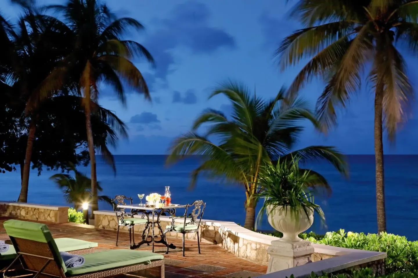 Oceanfront terrace with lounge chairs and a small table at dusk at Half Moon.