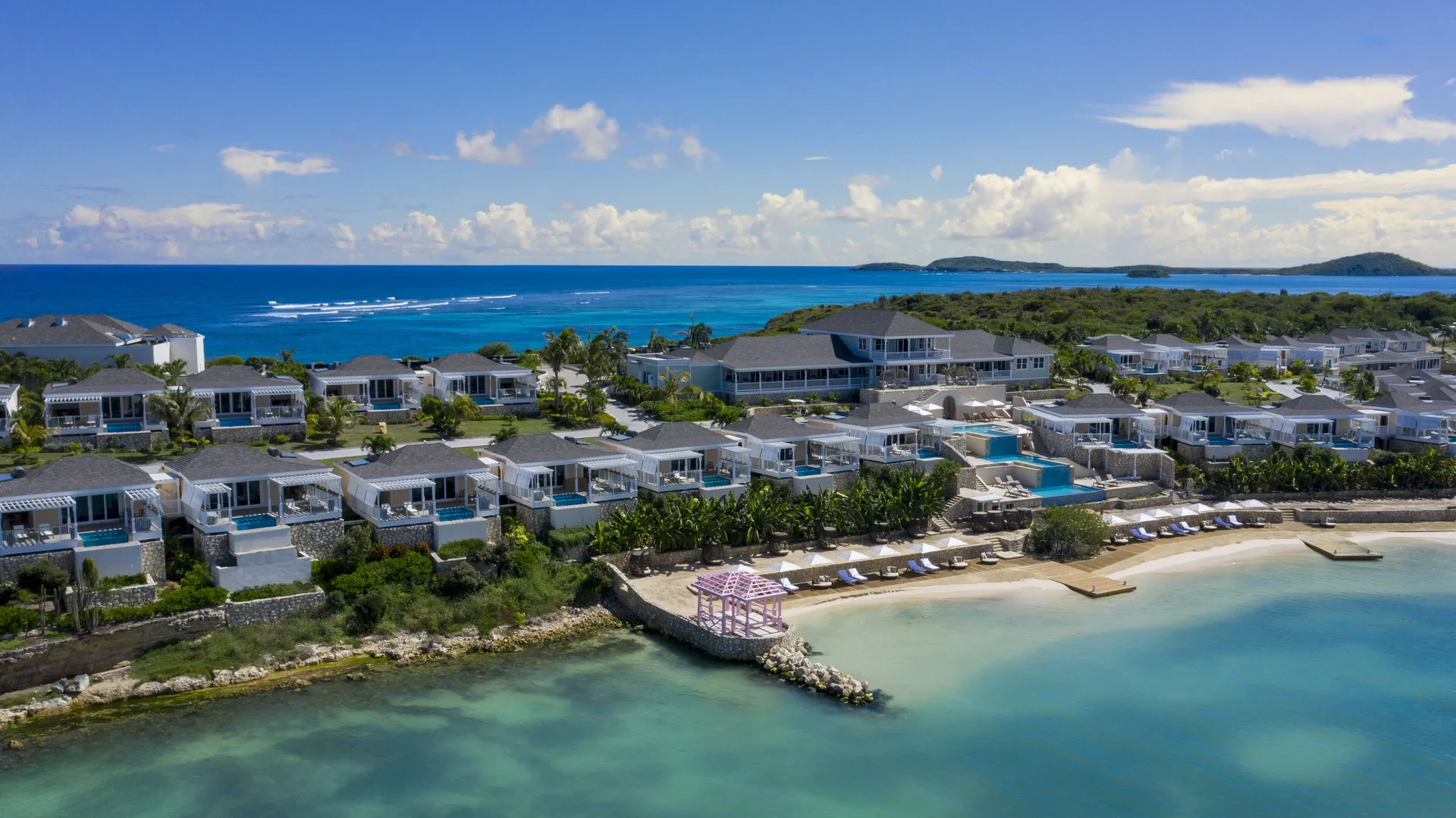 Aerial view of villas, beach, cove, and ocean at Hammock Cove Antigua.