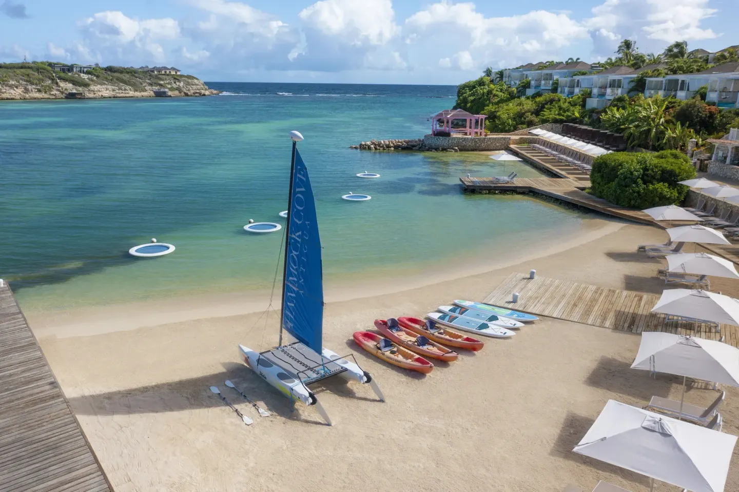 Beach cove with a sailboat, kayaks, umbrellas and hillside suites at Hammock Cove Antigua.