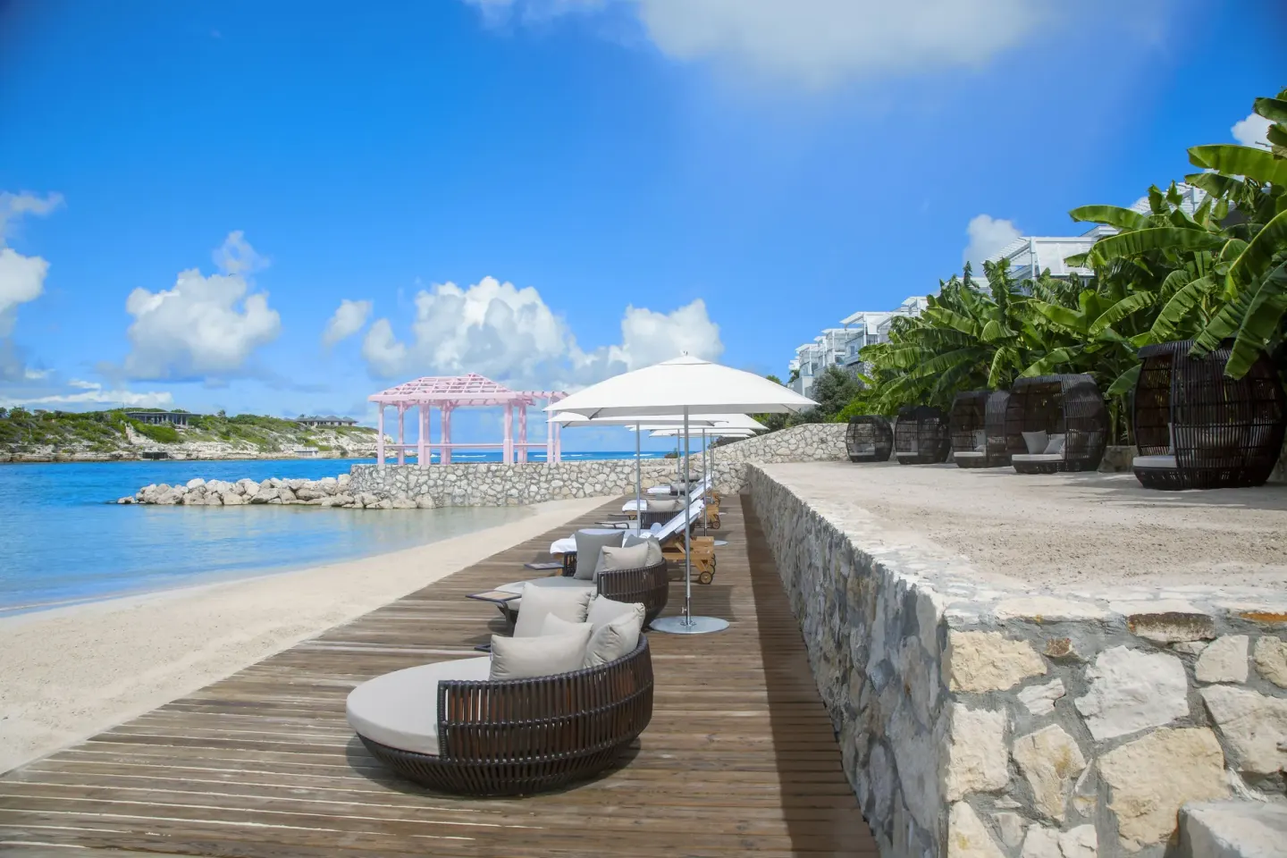 Beach loungers, umbrellas, and a pink gazebo by the water at Hammock Cove Antigua.