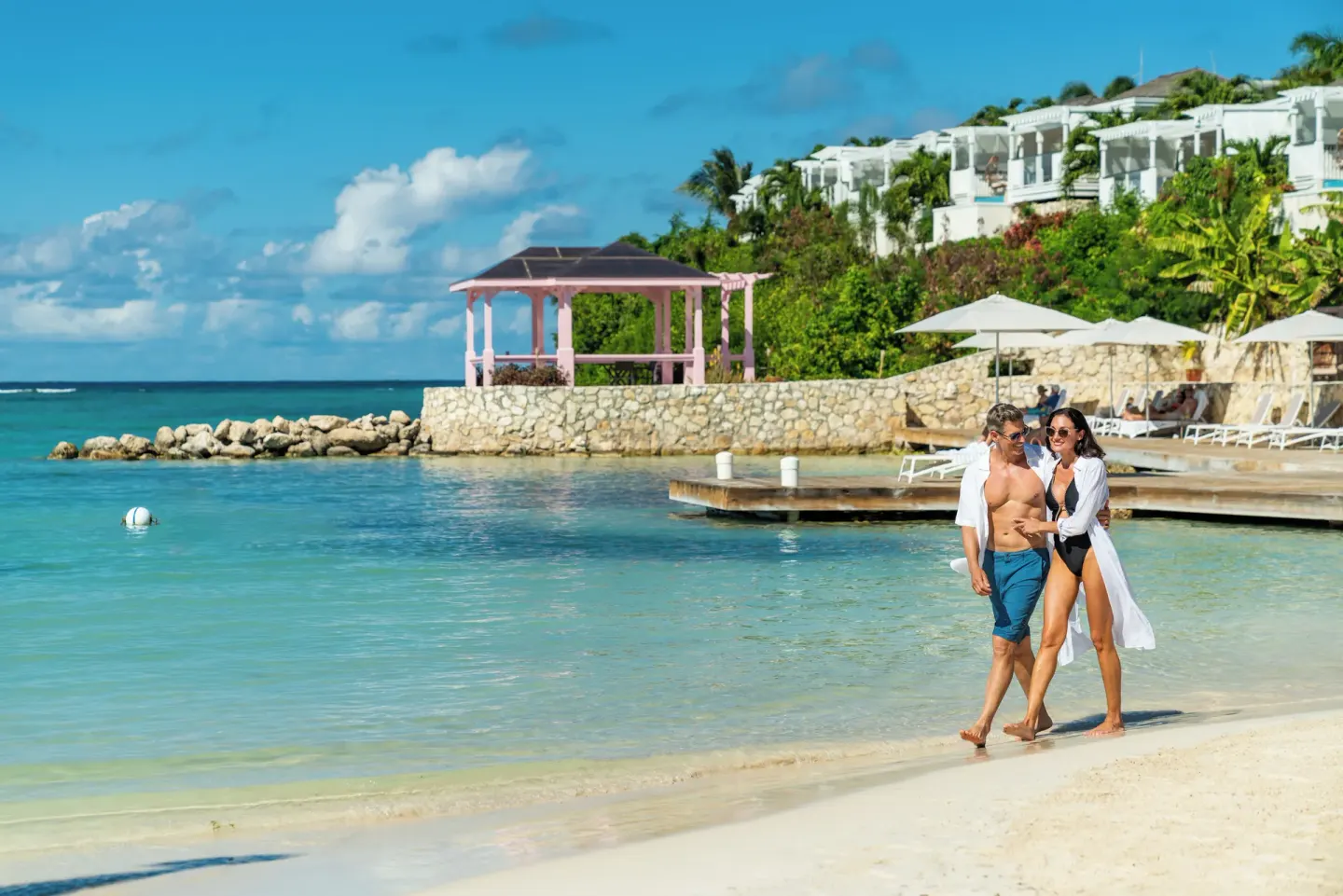 Couple walking along the calm beach with a pink gazebo at Hammock Cove Antigua.