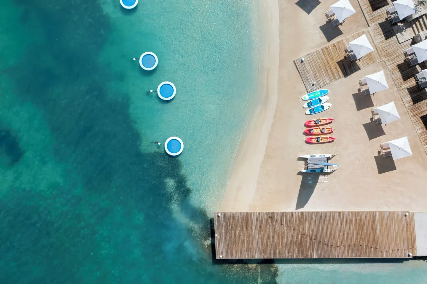 Straight-down aerial view of the beach, pier, umbrellas and water floats at Hammock Cove Antigua.