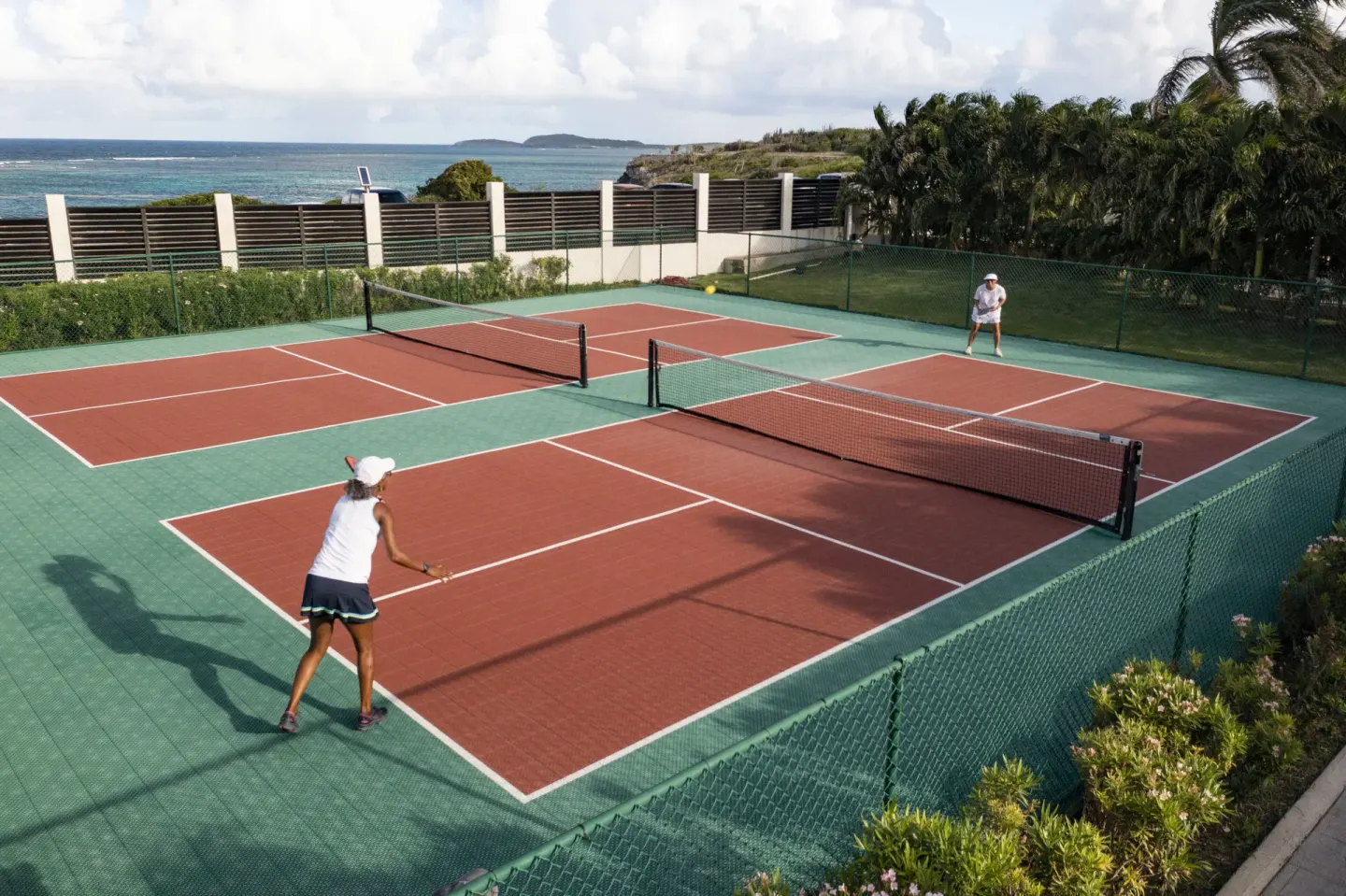 Tennis courts with two players and ocean beyond at Hammock Cove Antigua.
