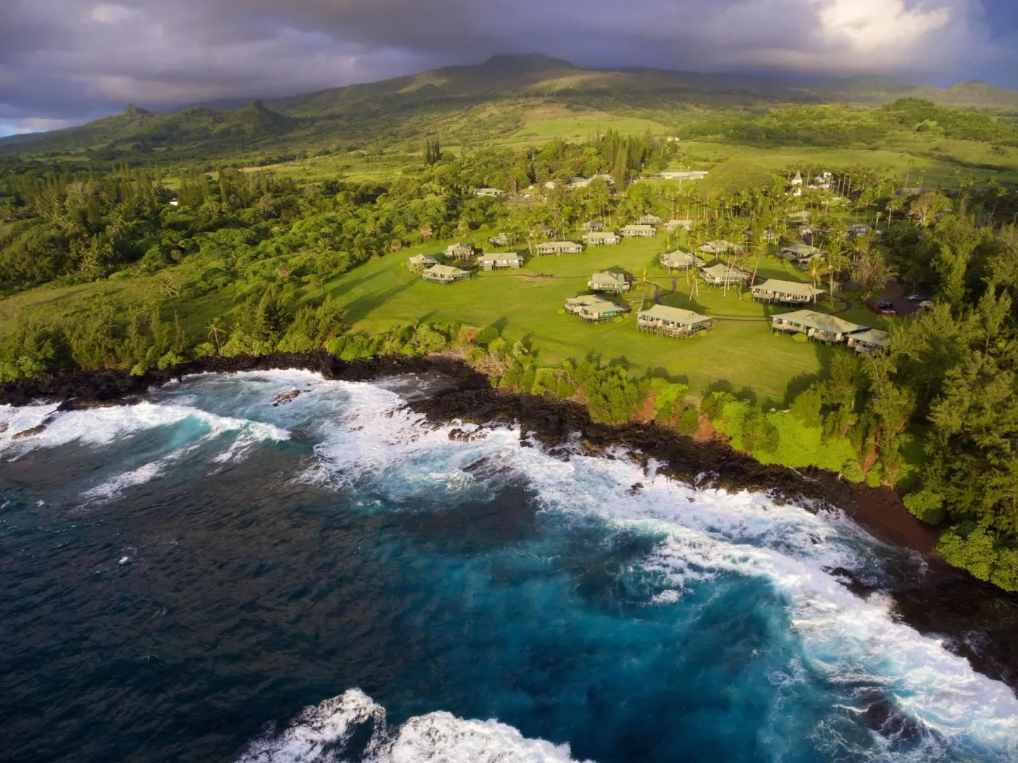 Aerial view of Hana-Maui Resort beside a rocky coastline and green hills.