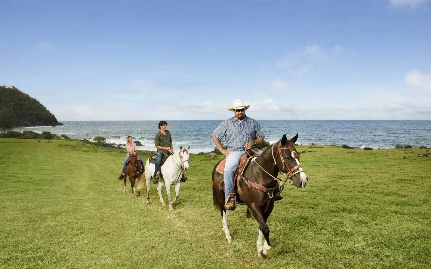 Horseback riders cross a grassy coastal field near Hana-Maui Resort.