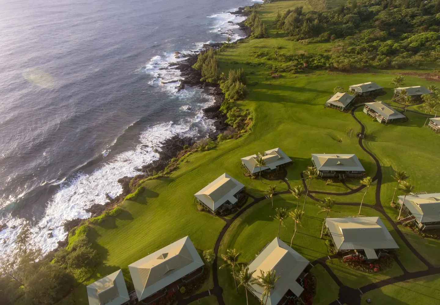 Aerial view of cottages, lawns, and winding paths beside the ocean at Hana-Maui Resort.
