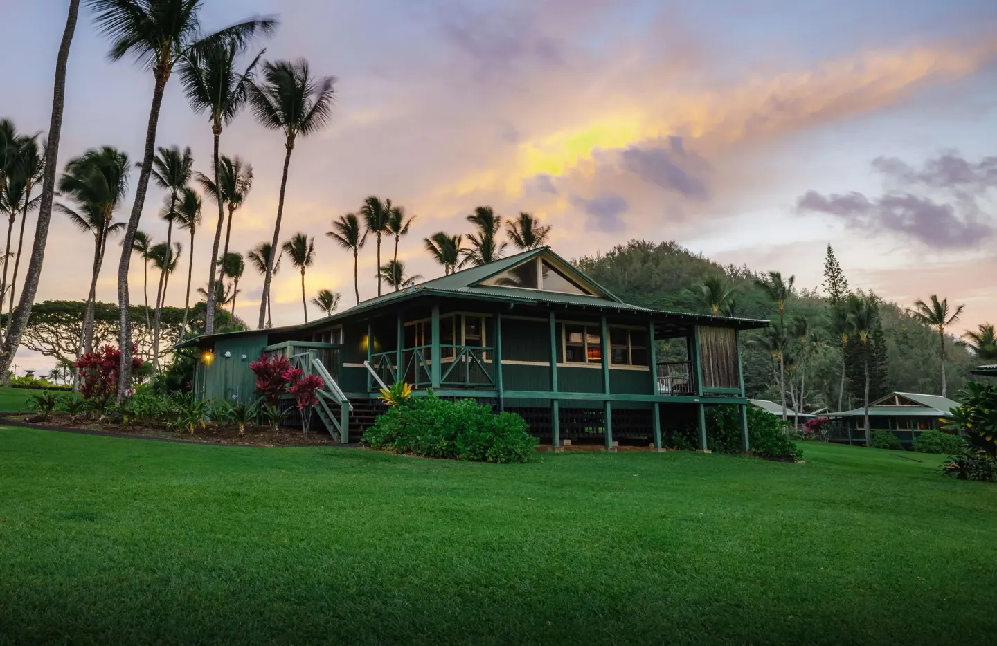A cottage on a green lawn with palm trees at dusk at Hana-Maui Resort.