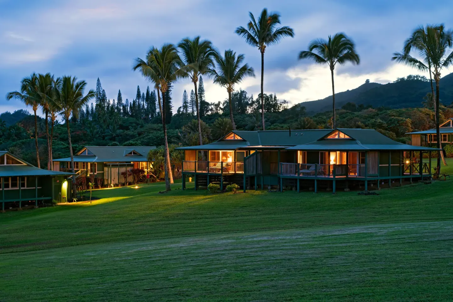 Guest bungalows with lit windows on green lawns at Hana-Maui Resort.