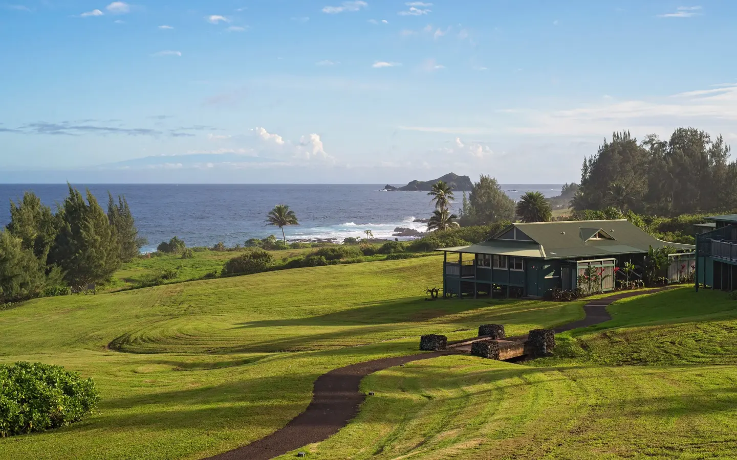 Grassy resort grounds with a cottage and ocean beyond at Hana-Maui Resort.