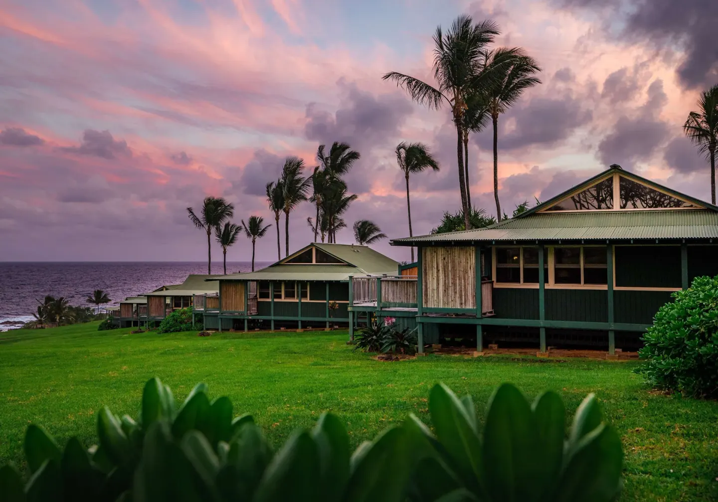 Oceanfront cottages and palms at sunset on the grounds of Hana-Maui Resort.