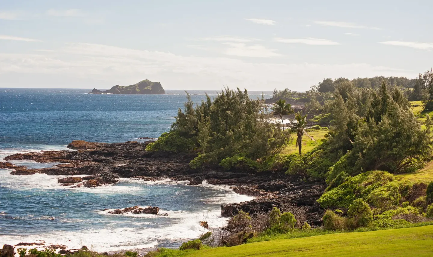 Rocky shoreline, trees, and blue ocean near the grounds at Hana-Maui Resort.