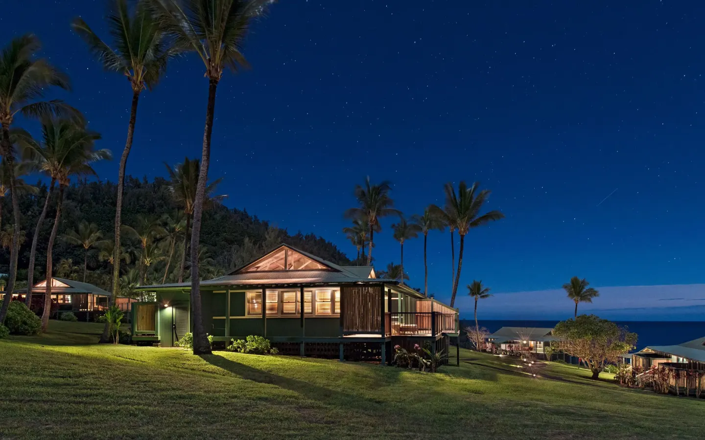 Illuminated bungalow and palm trees under a starry sky at Hana-Maui Resort.