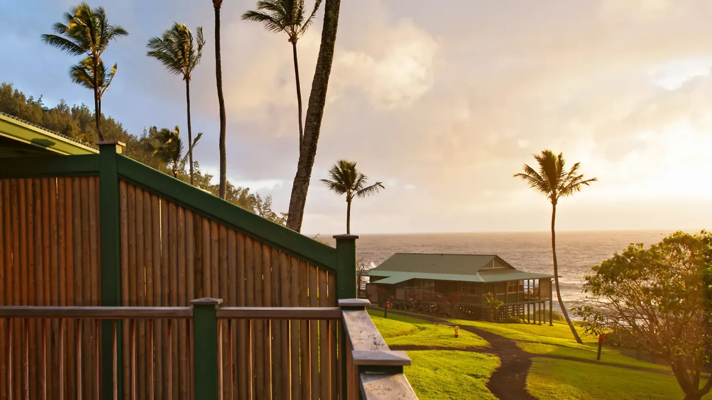 Palm trees, a walkway, and oceanfront cottage in golden light at Hana-Maui Resort.