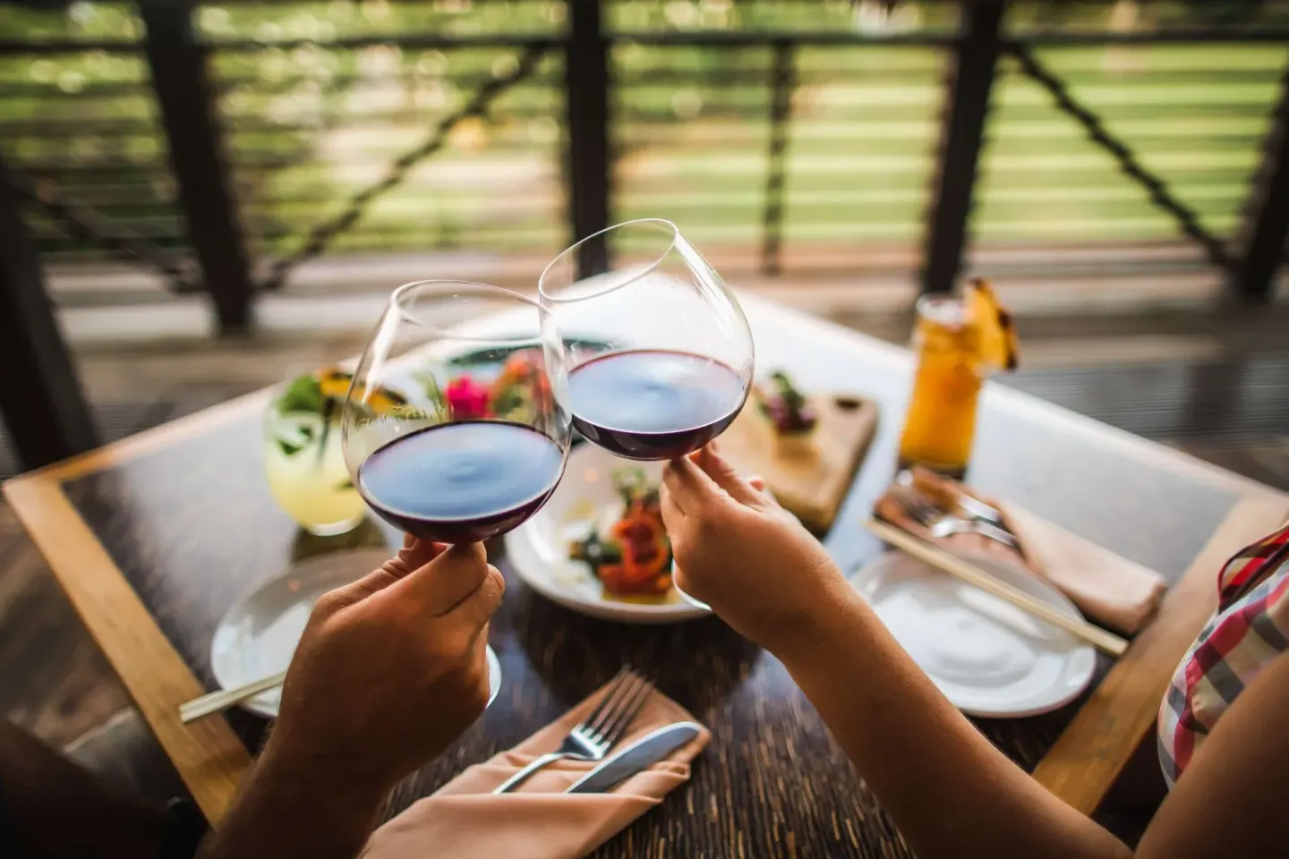 Two guests toast red wine over a table of food and drinks at Hana-Maui Resort.