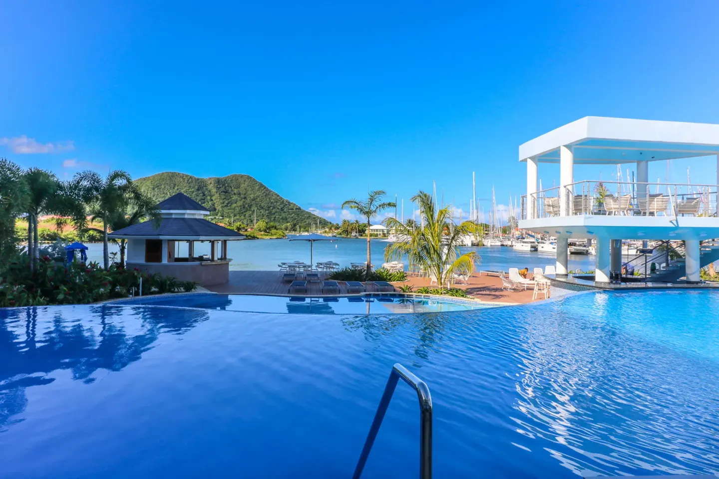 Infinity pool with marina, white deck, palms, and hills at Harbor Club St. Lucia.