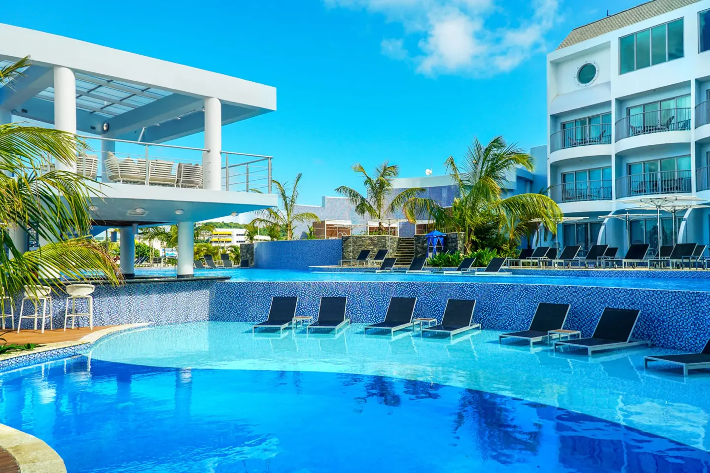 Multi-level pool with in-water loungers, palms, and balconies at Harbor Club St. Lucia.