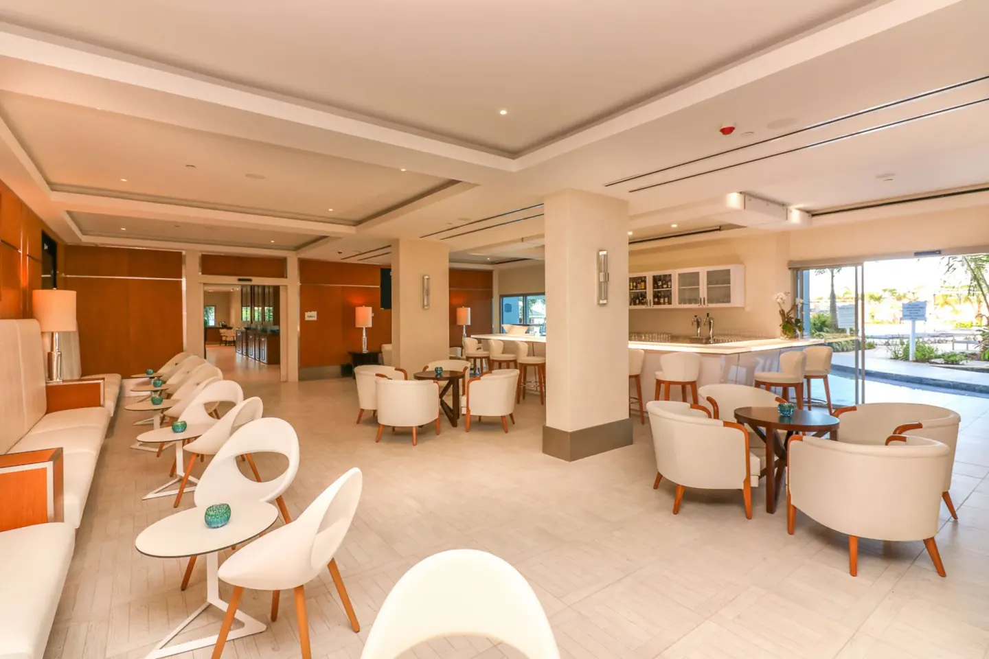 Open lounge with white seating, small tables, and a bar at Harbor Club St. Lucia.