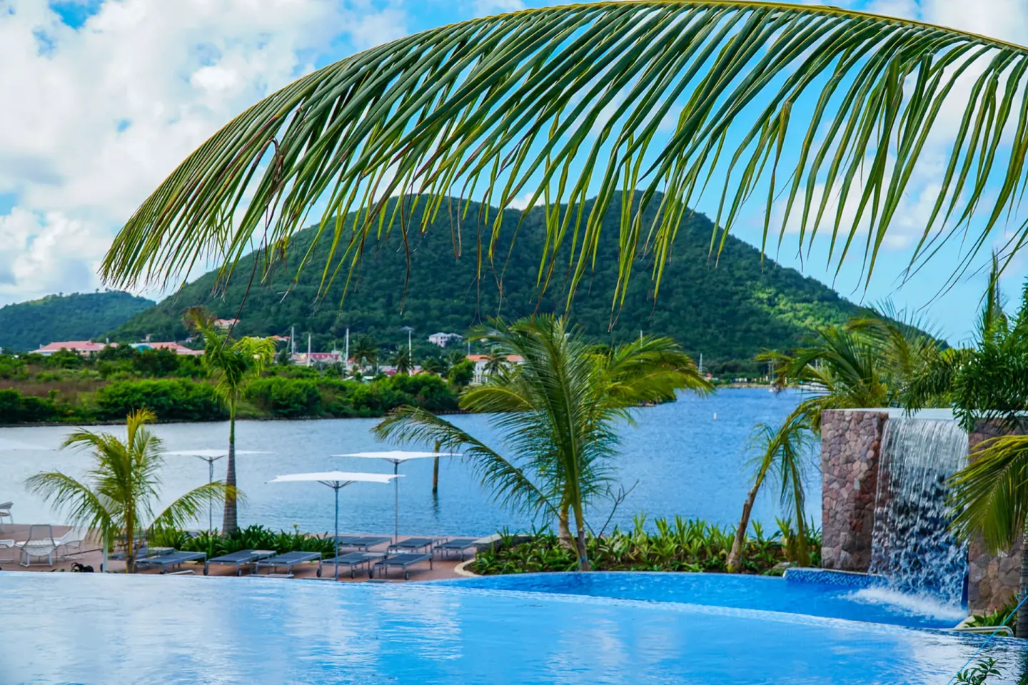 Pool edge with waterfall feature, palms, lagoon, and hillside at Harbor Club St. Lucia.