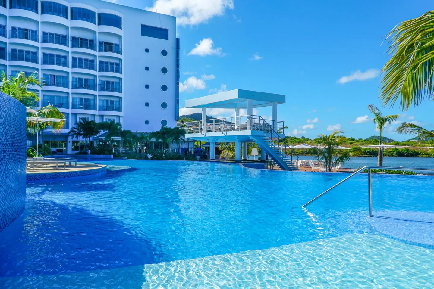 Sunny resort pool with hotel building and harbor beyond at Harbor Club St. Lucia.