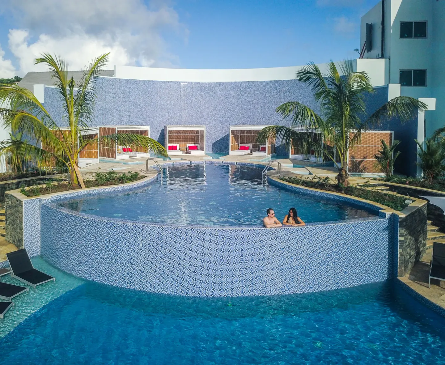 Tiered pool with cabanas, palm trees, and two guests at Harbor Club St. Lucia.
