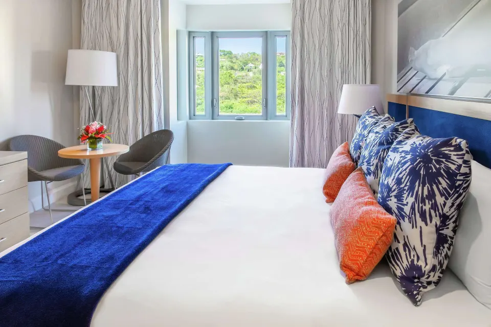Island View king bed beside a window with greenery outside at Harbor Club St. Lucia.