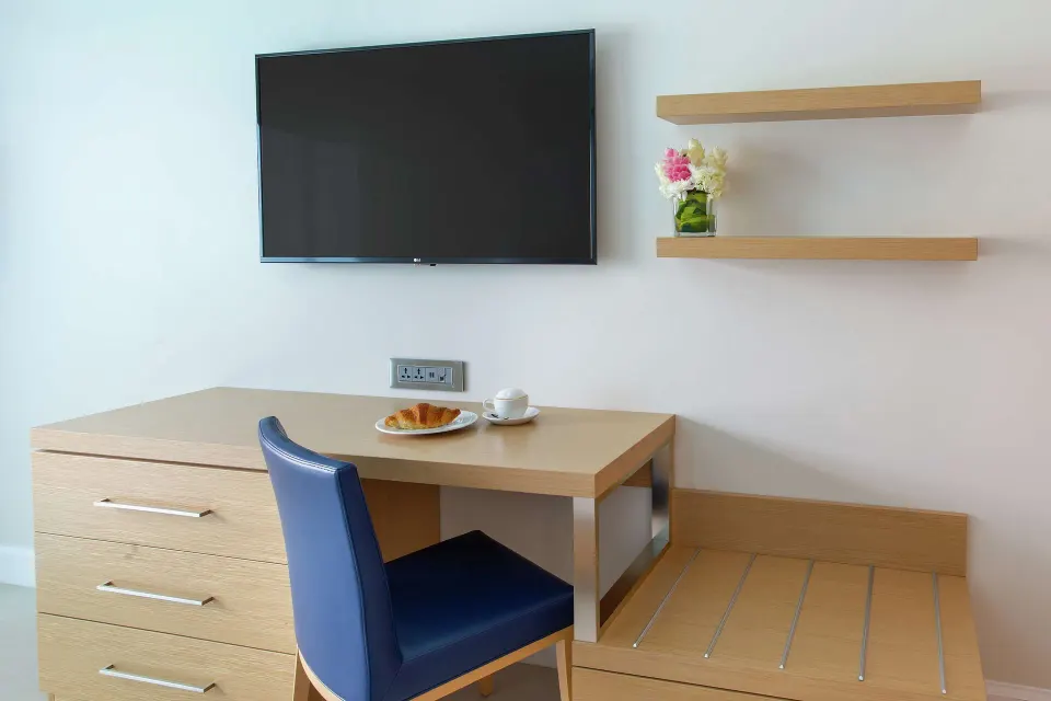 Desk, dresser, luggage bench, and wall TV in a guest room at Harbor Club St. Lucia.