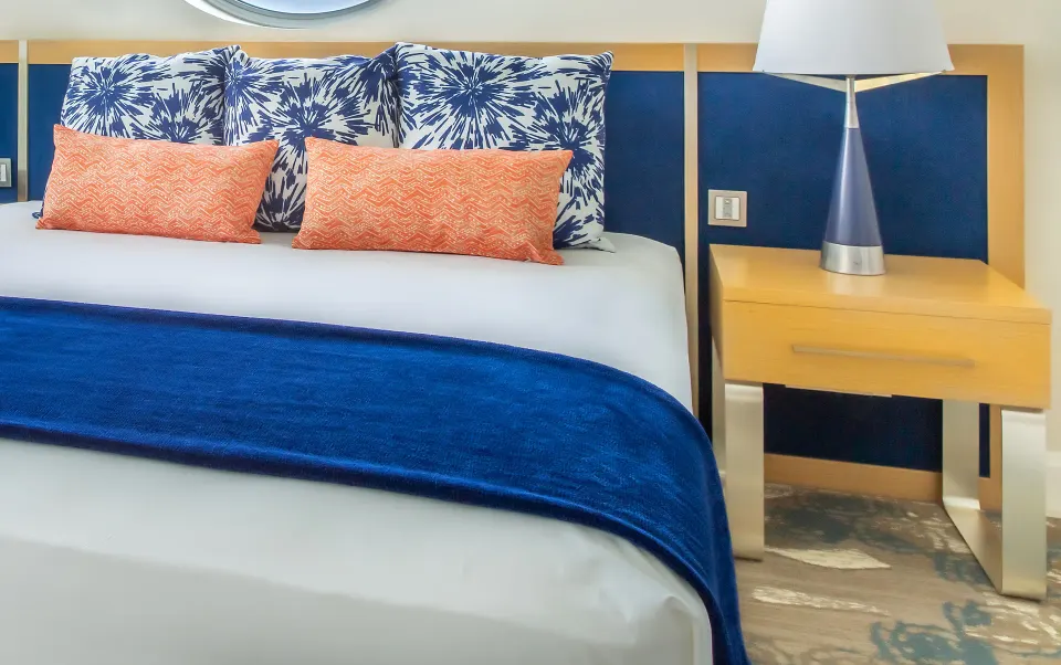 King bed with blue throw and patterned pillows in a guest room at Harbor Club St. Lucia.