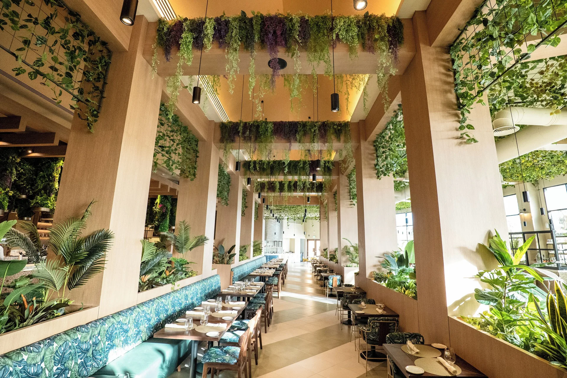 Plant-filled dining room at Hard Rock Hotel & Casino Punta Cana with long banquettes and set tables.