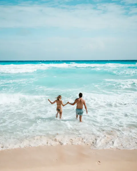 Two people holding hands in the surf by the beach at Hard Rock Hotel Cancun.