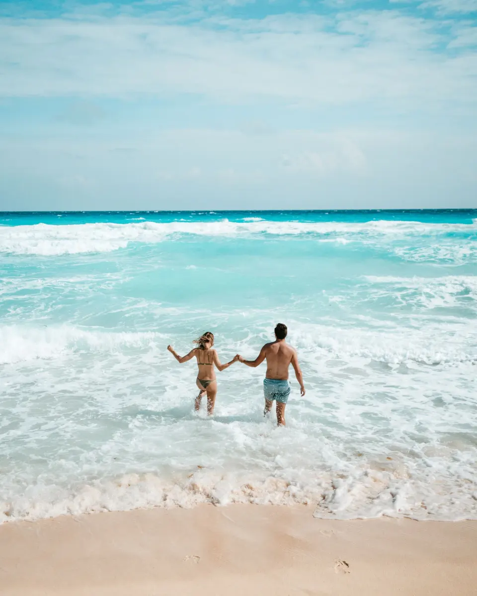 Two people holding hands in the surf by the beach at Hard Rock Hotel Cancun.