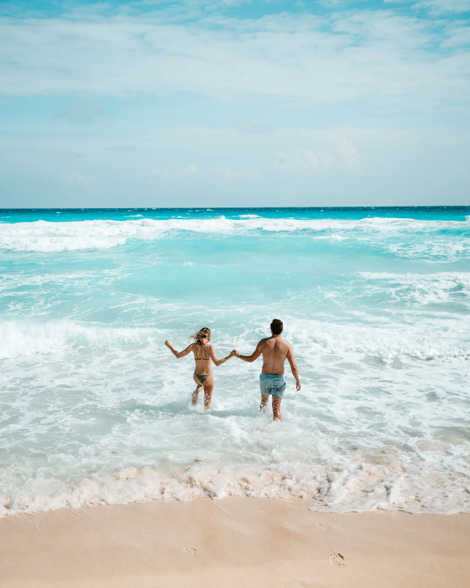 Two people holding hands in the surf by the beach at Hard Rock Hotel Cancun.