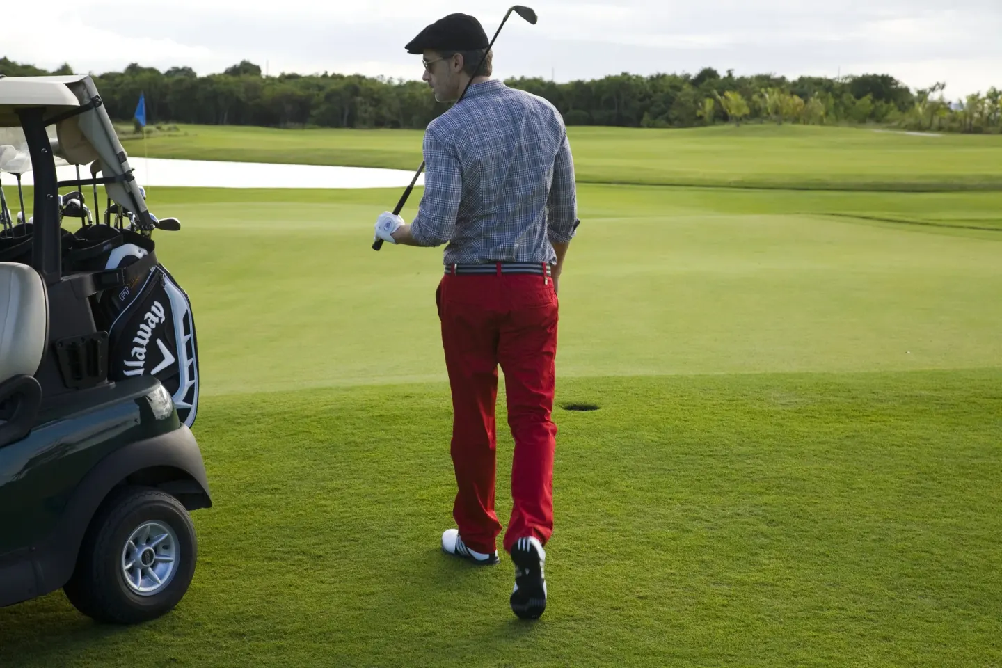 A golfer walks beside a cart on a green course near Hard Rock Hotel Cancun.