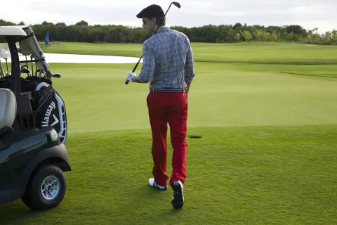 A golfer walks beside a cart on a green course near Hard Rock Hotel Cancun.