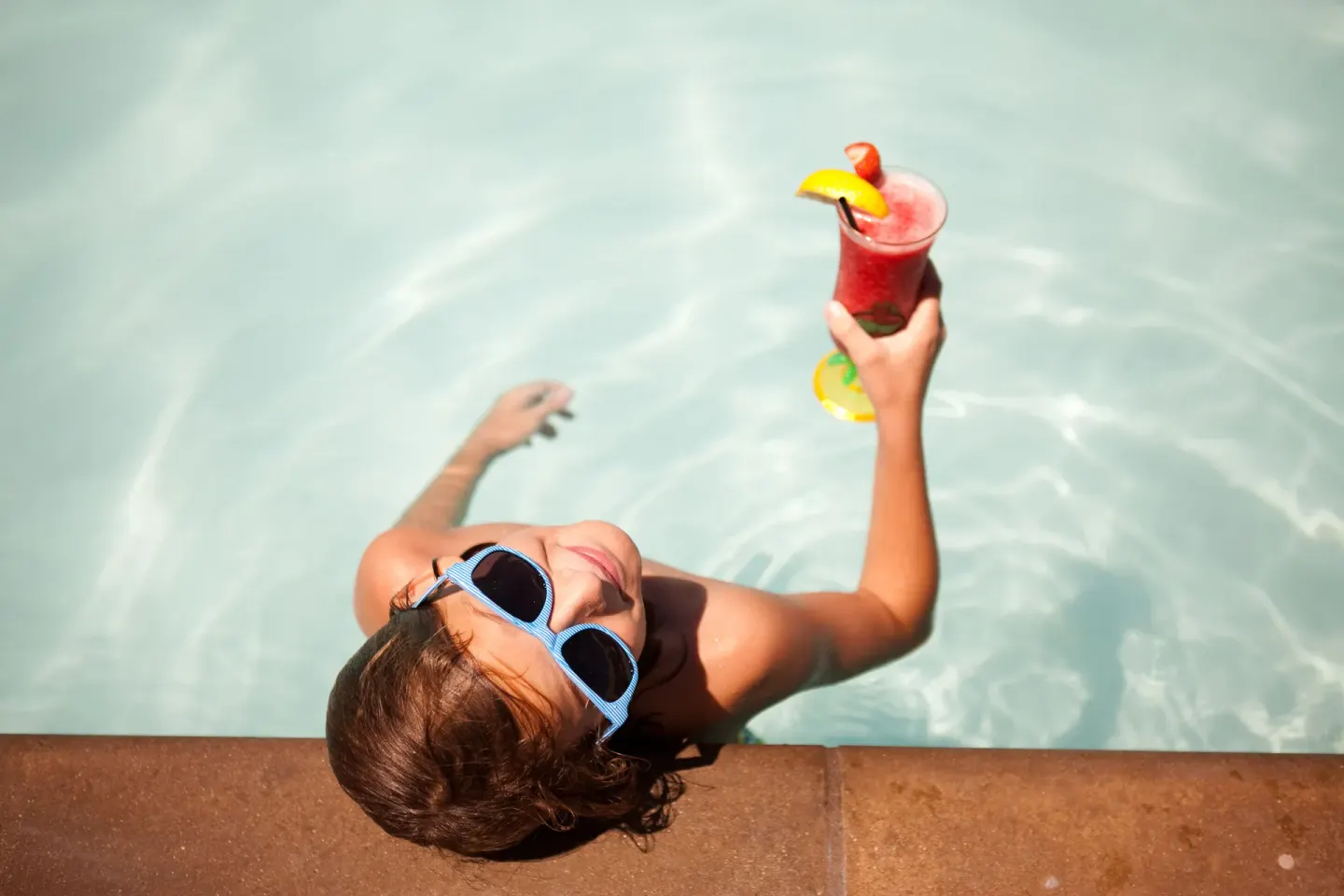 Guest in sunglasses holds a tropical drink in the pool at Hard Rock Hotel Cancun.
