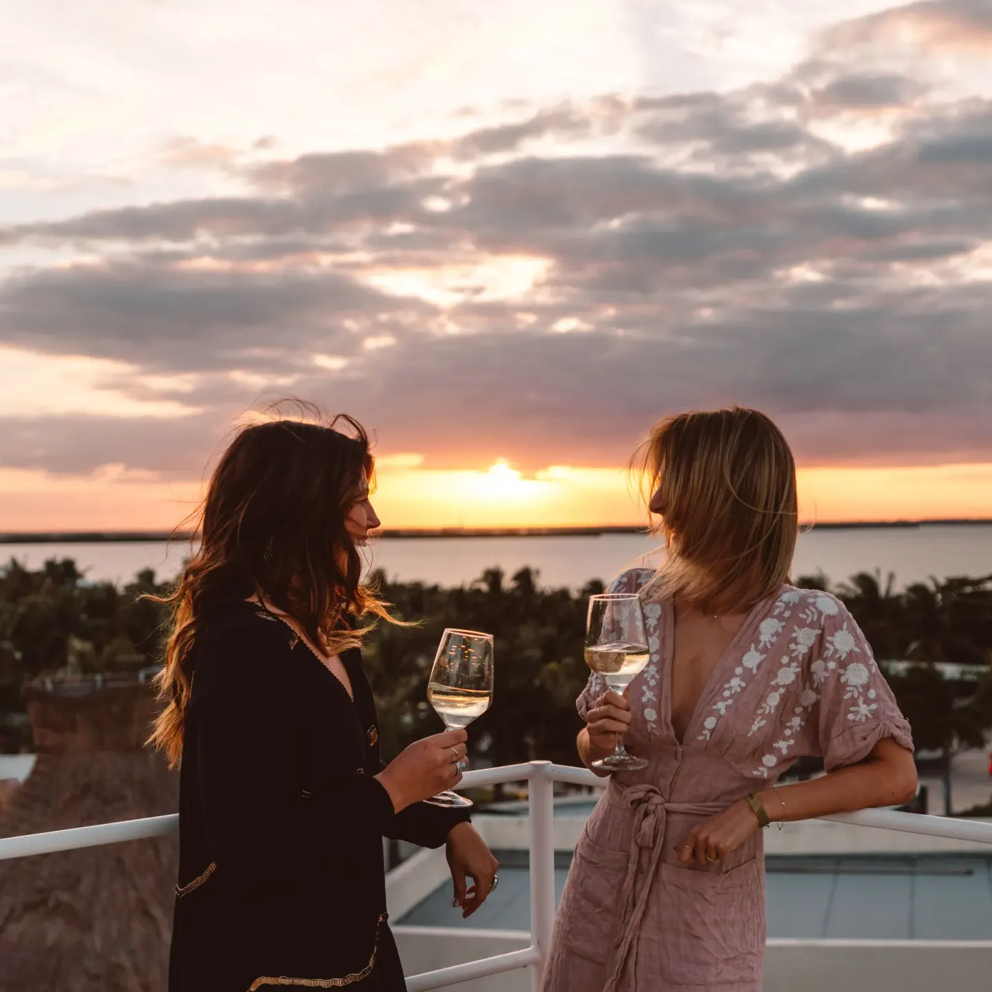Two guests holding wine glasses on a terrace at sunset at Hard Rock Hotel Cancun.