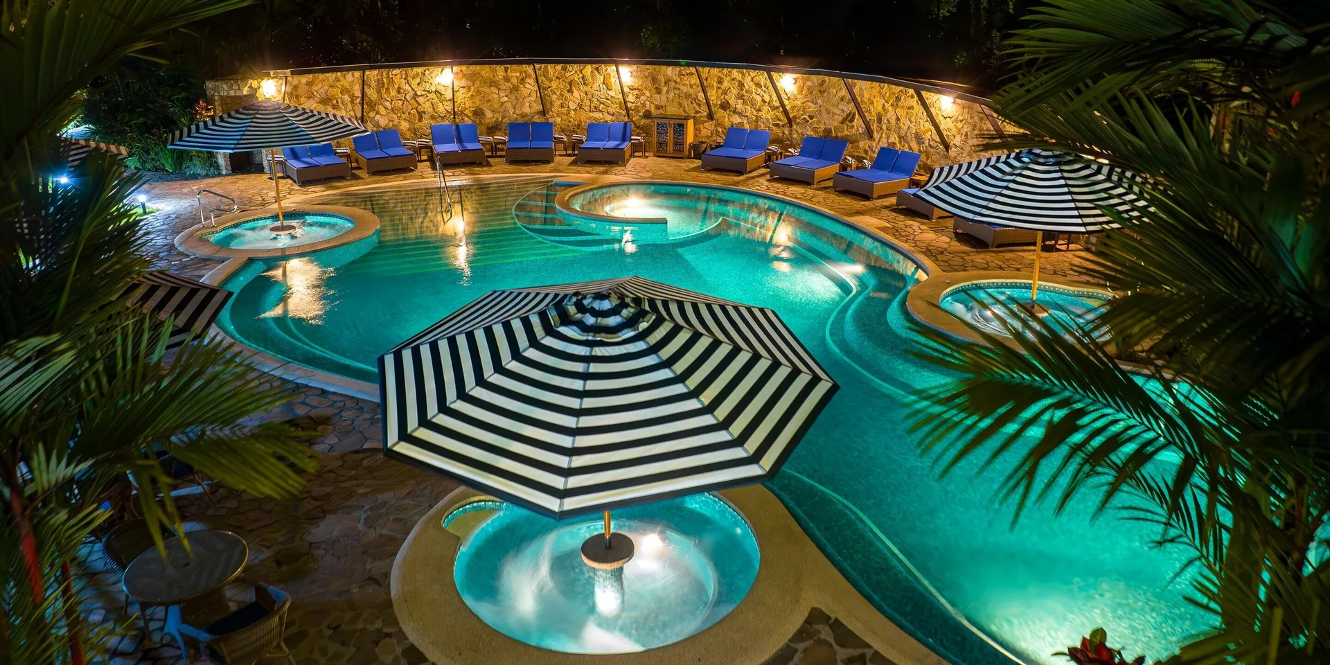 Nighttime pool with striped umbrellas and blue loungers at Hideaway Rio Celeste.