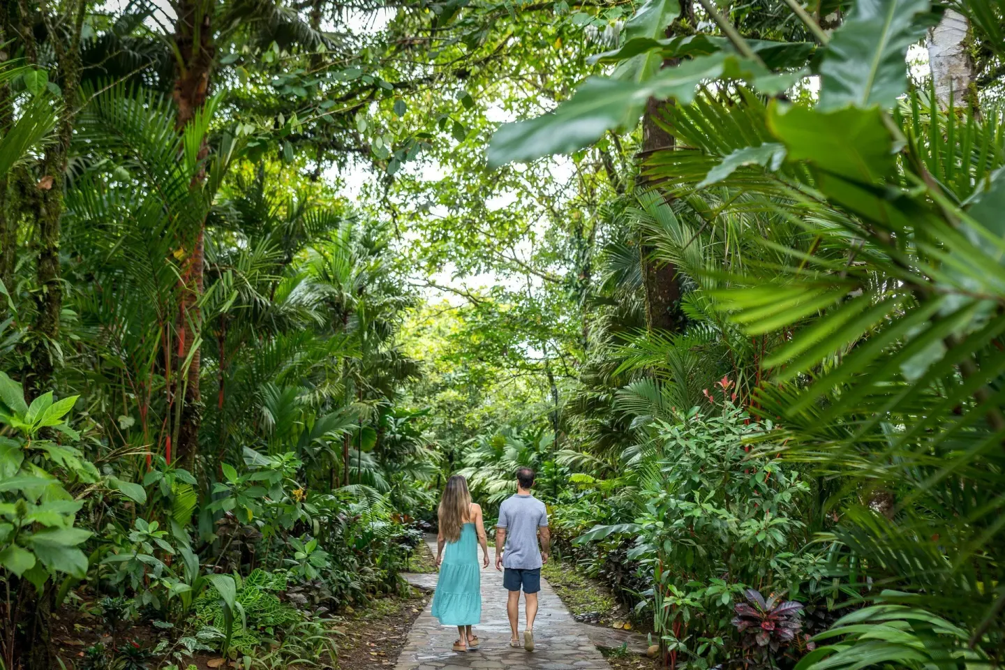 Couple walking a stone path through tropical gardens at Hideaway Rio Celeste.
