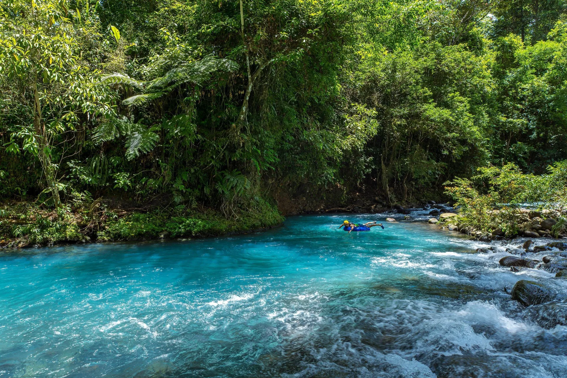 A swimmer floats in bright turquoise river water near Hideaway Rio Celeste.