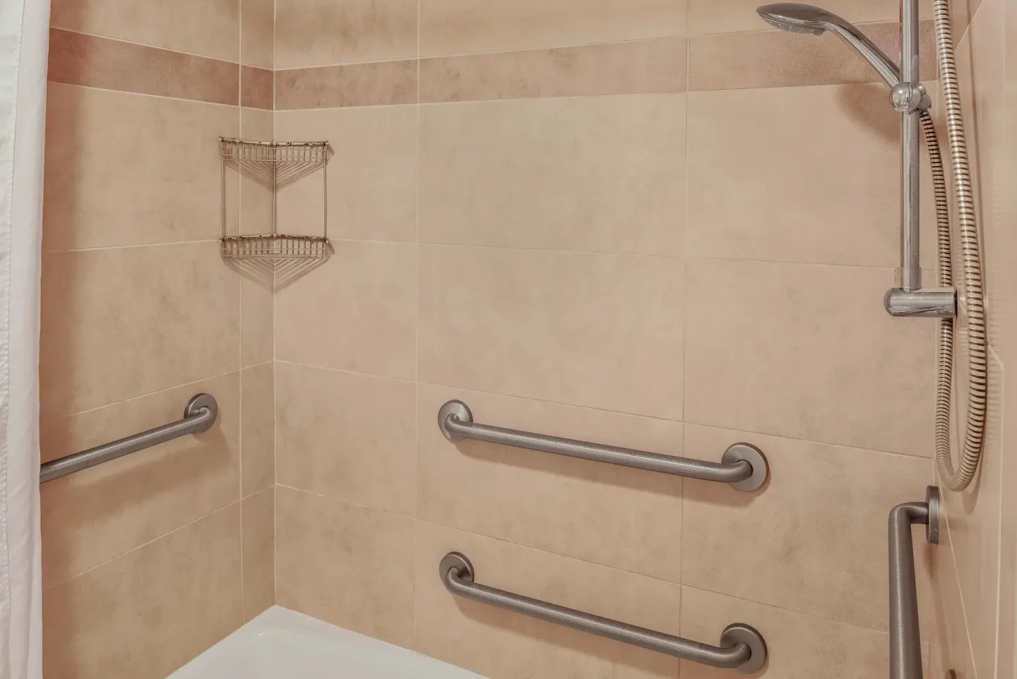 Tiled shower with handheld showerhead and grab bars at Hilo Hawaiian Hotel.