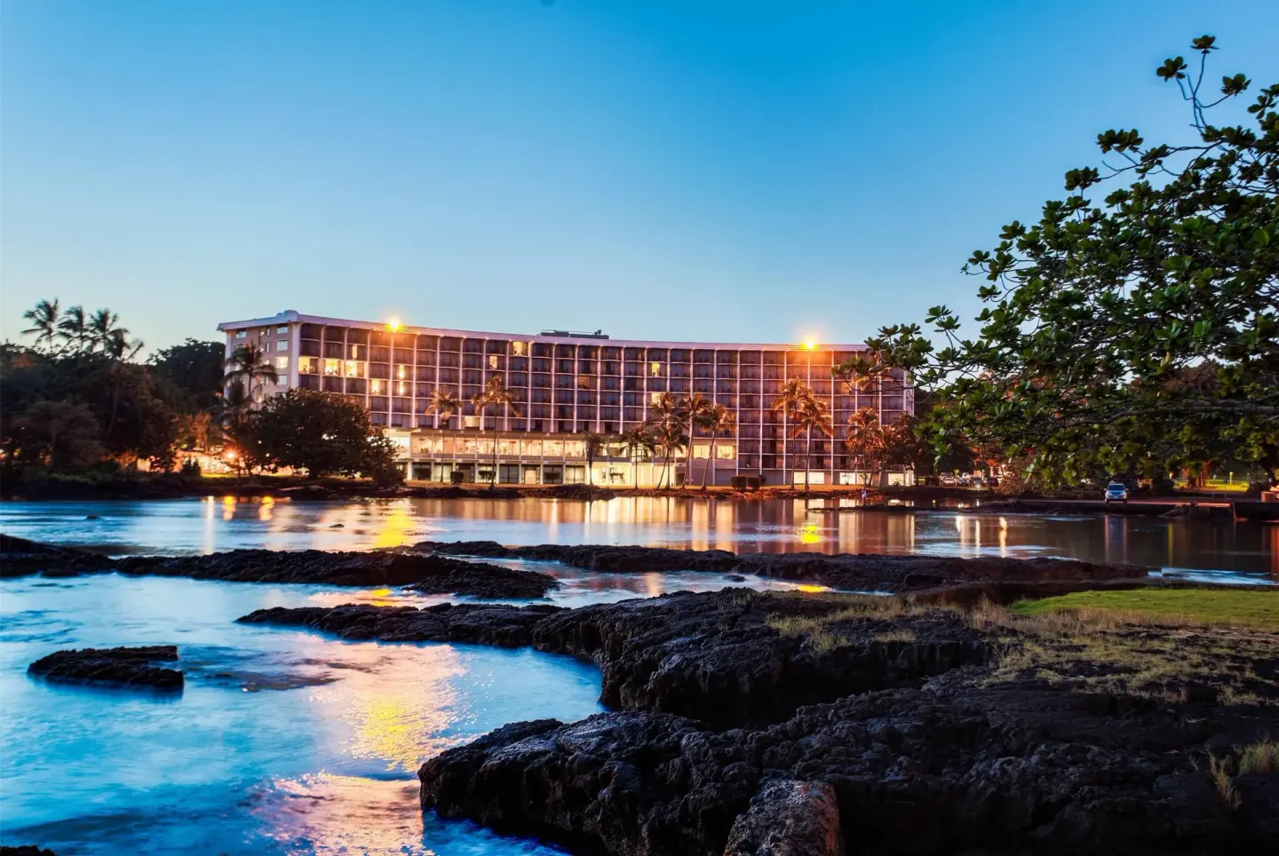 Evening waterfront view of the illuminated hotel building at Hilo Hawaiian Hotel.