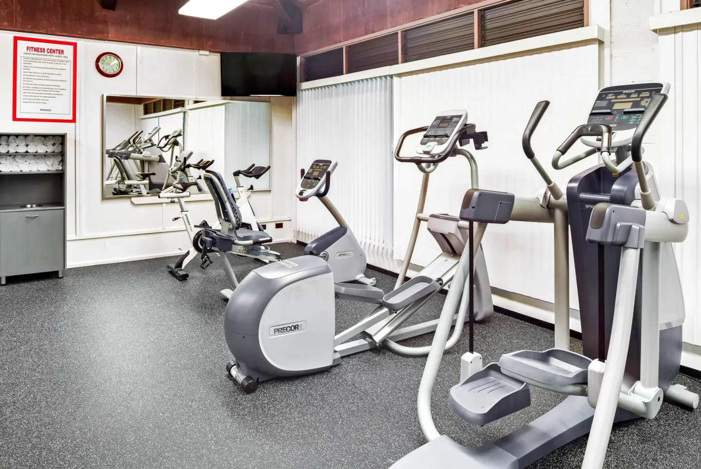 Fitness center with cardio machines, mirror, towels, and wall sign at Hilo Hawaiian Hotel.