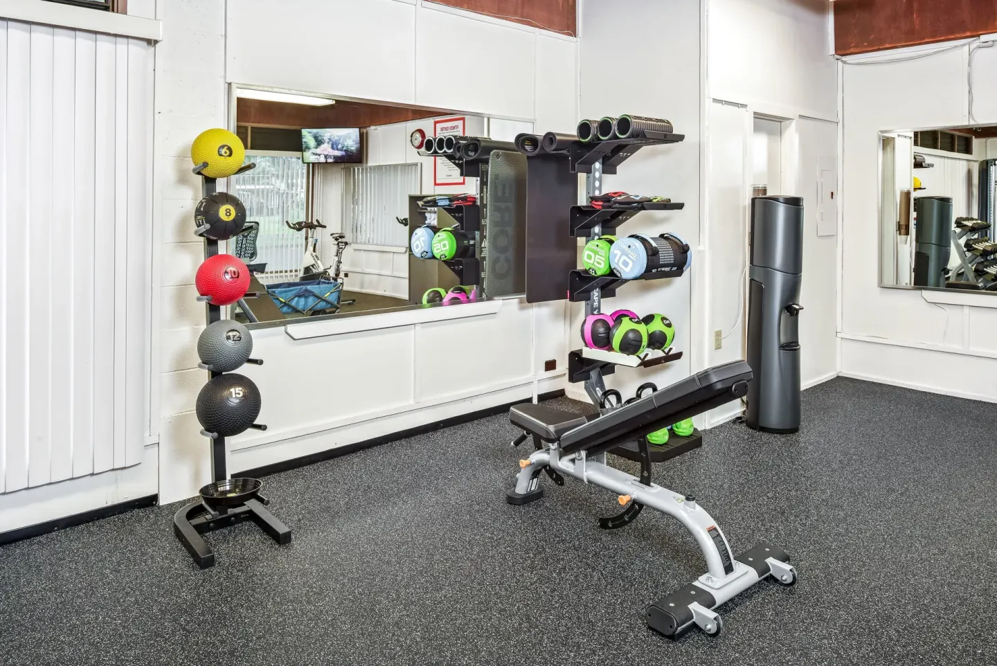 Fitness room with bench, medicine balls, weights, and mirrors at Hilo Hawaiian Hotel.