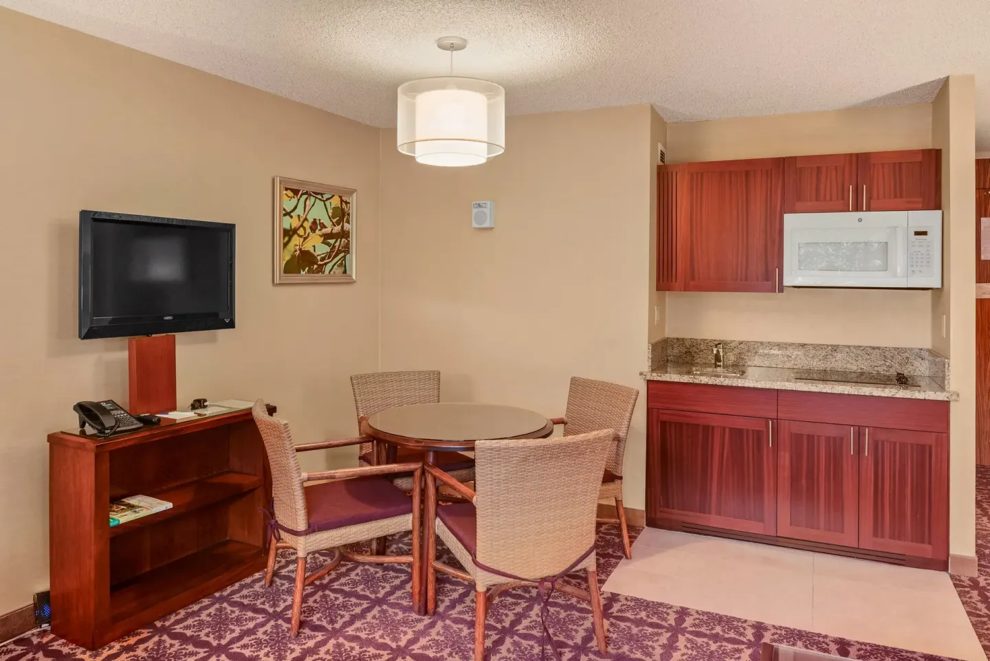 Guest room dining area with kitchenette and wall-mounted TV at Hilo Hawaiian Hotel.