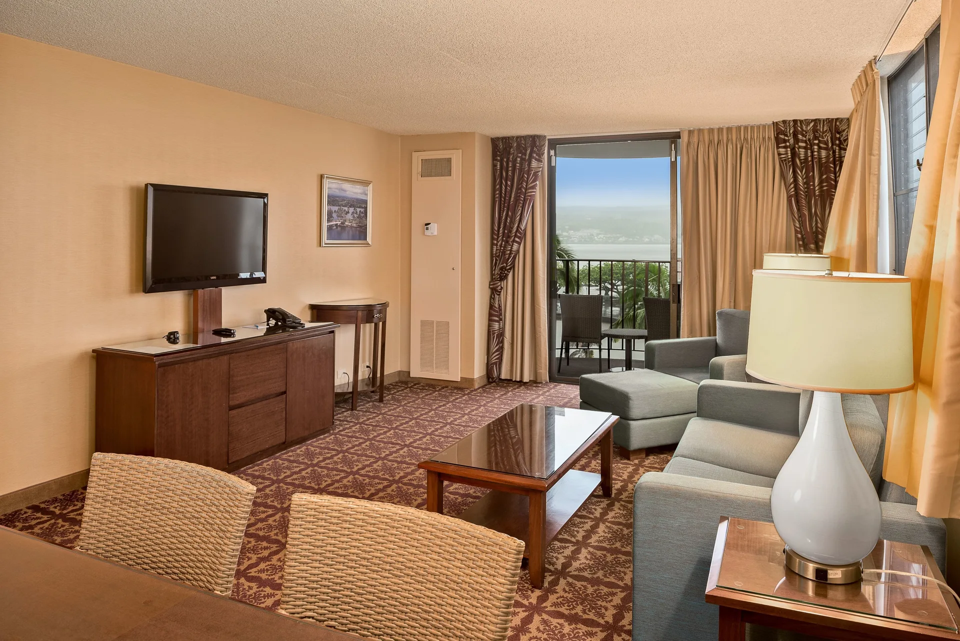 Living area with sofa, TV, and balcony beyond at Hilo Hawaiian Hotel.