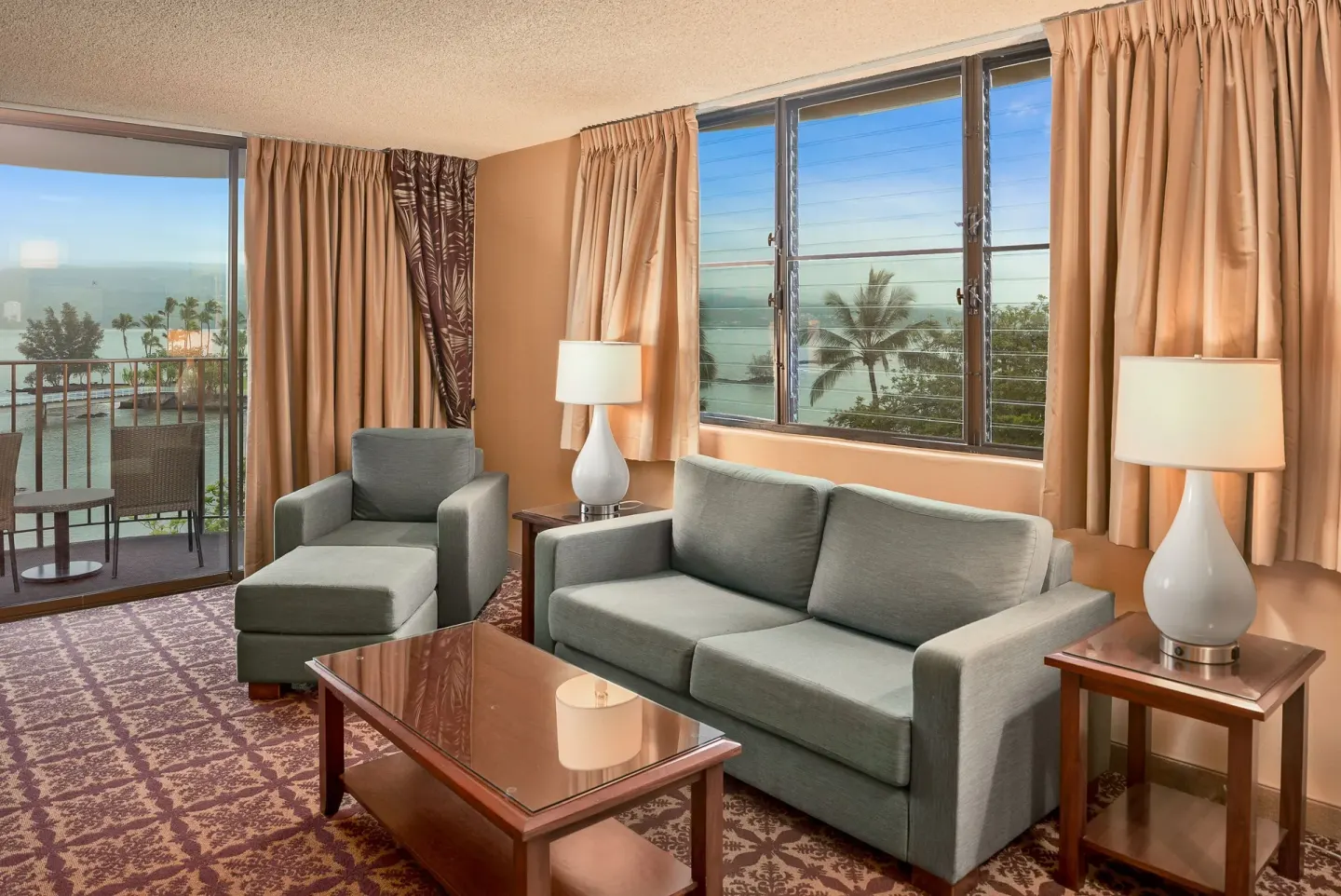 Guest room sitting area with sofa, lounge chair, and water views at Hilo Hawaiian Hotel.