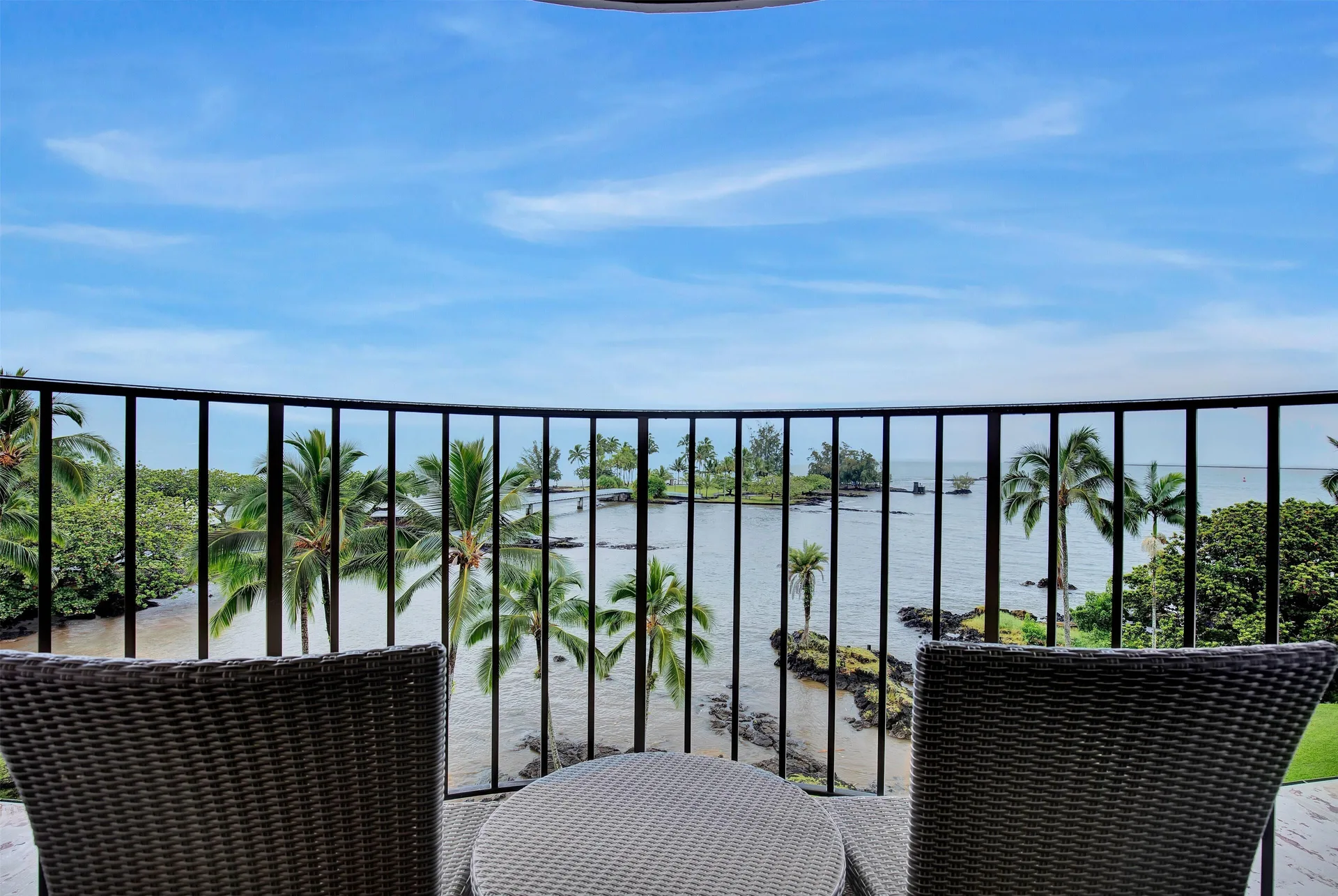 Balcony seating overlooking palms, shoreline, and ocean at Hilo Hawaiian Hotel.