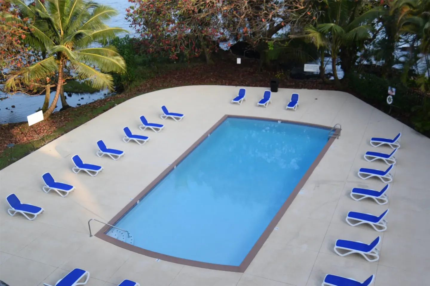 Outdoor pool with blue lounge chairs and tropical trees at Hilo Hawaiian Hotel.