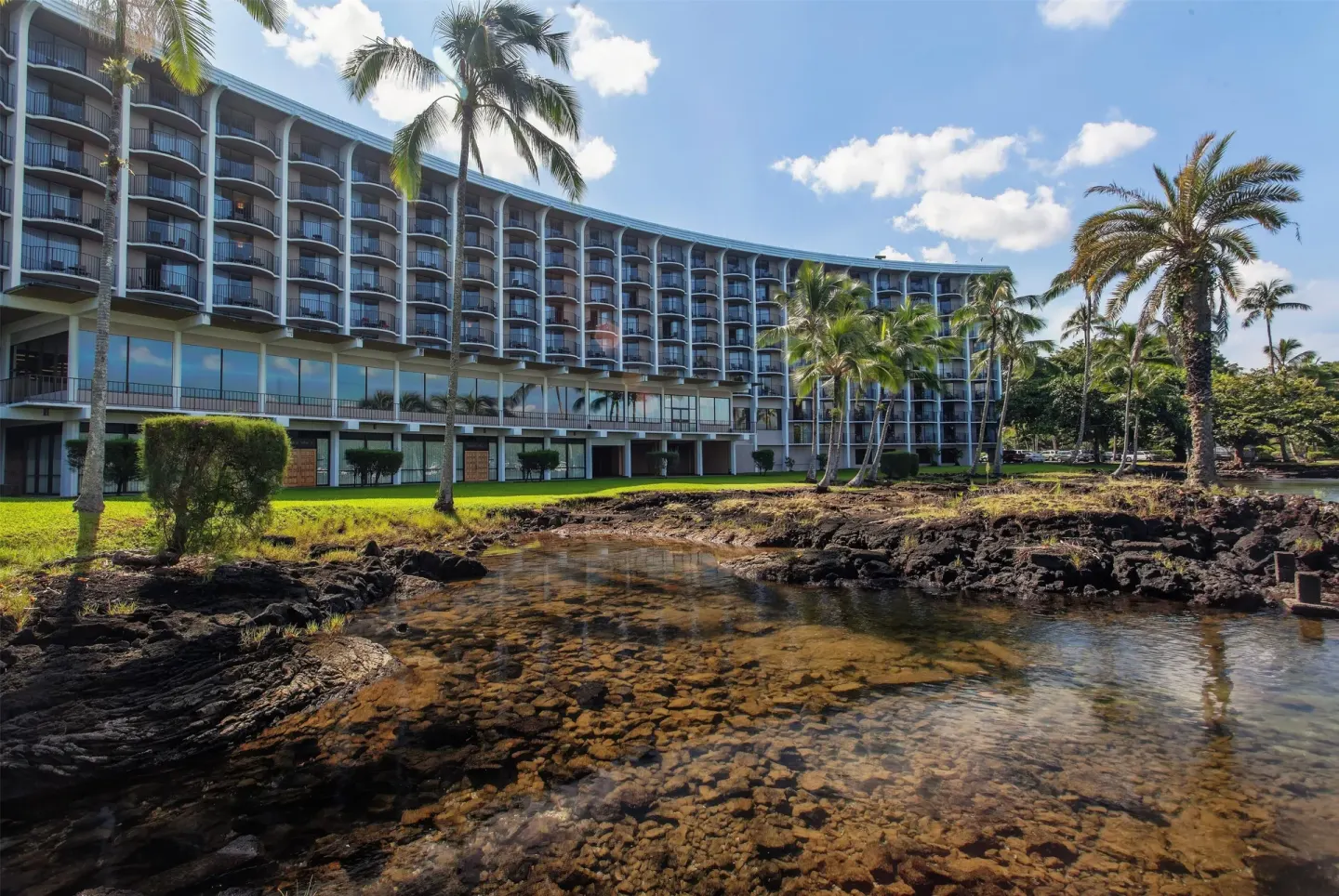Waterfront exterior with balconies, palms, and lava rock pools at Hilo Hawaiian Hotel.