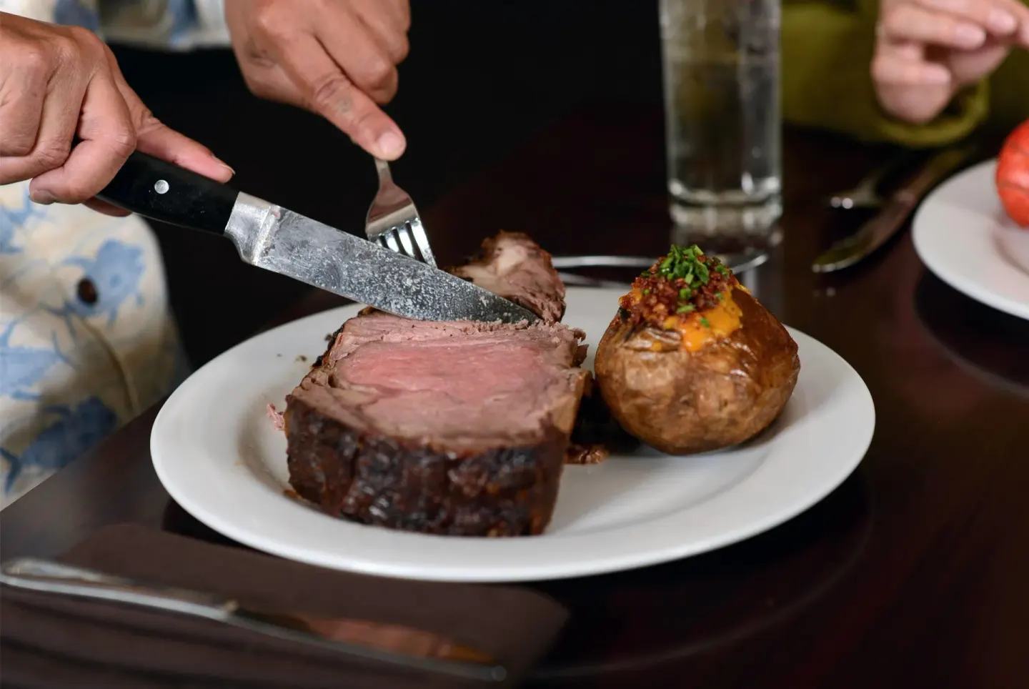 A steak dinner being cut beside a loaded baked potato at Hilo Hawaiian Hotel.